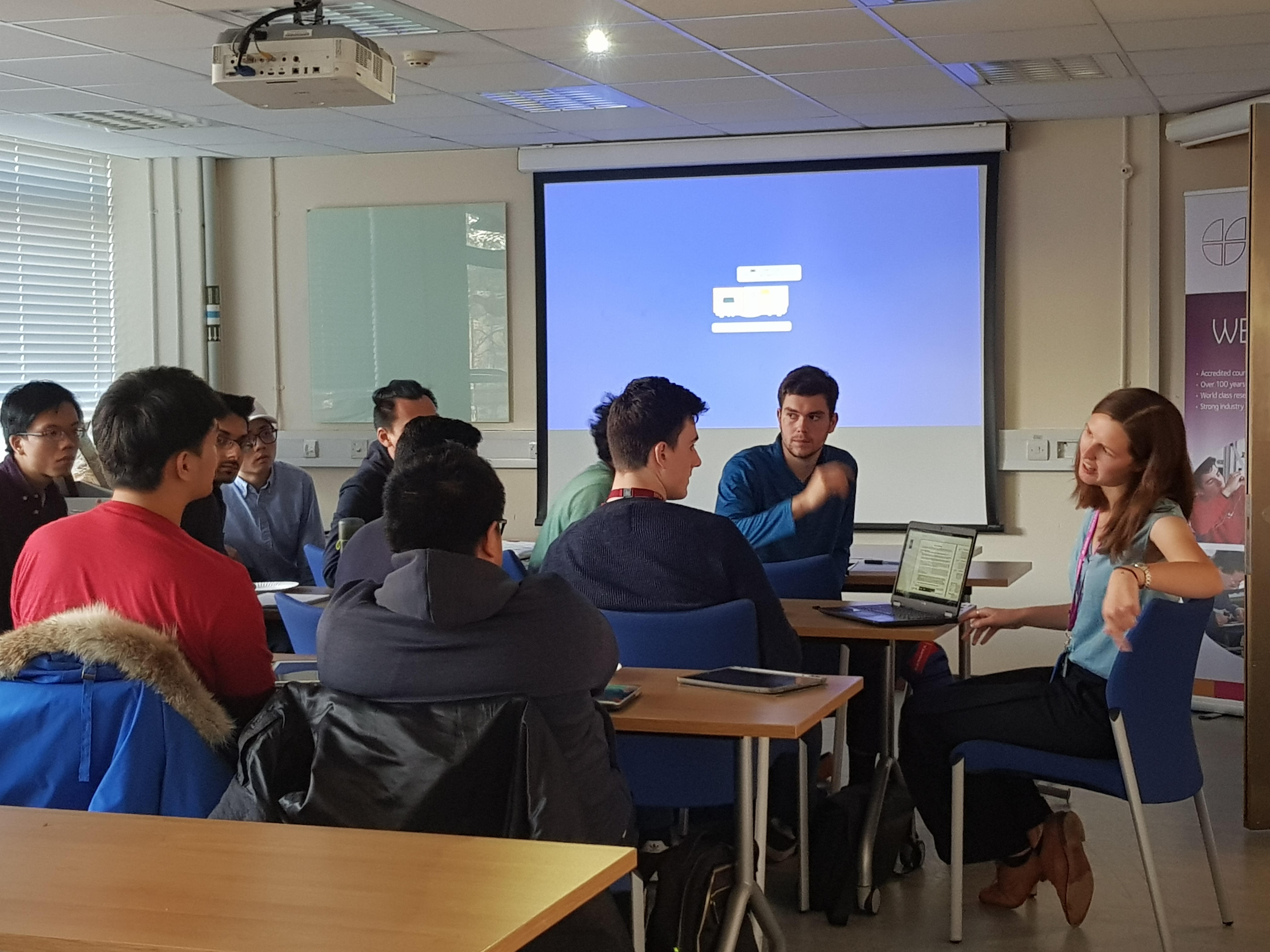 Students in classroom sat with teachers, discussing.