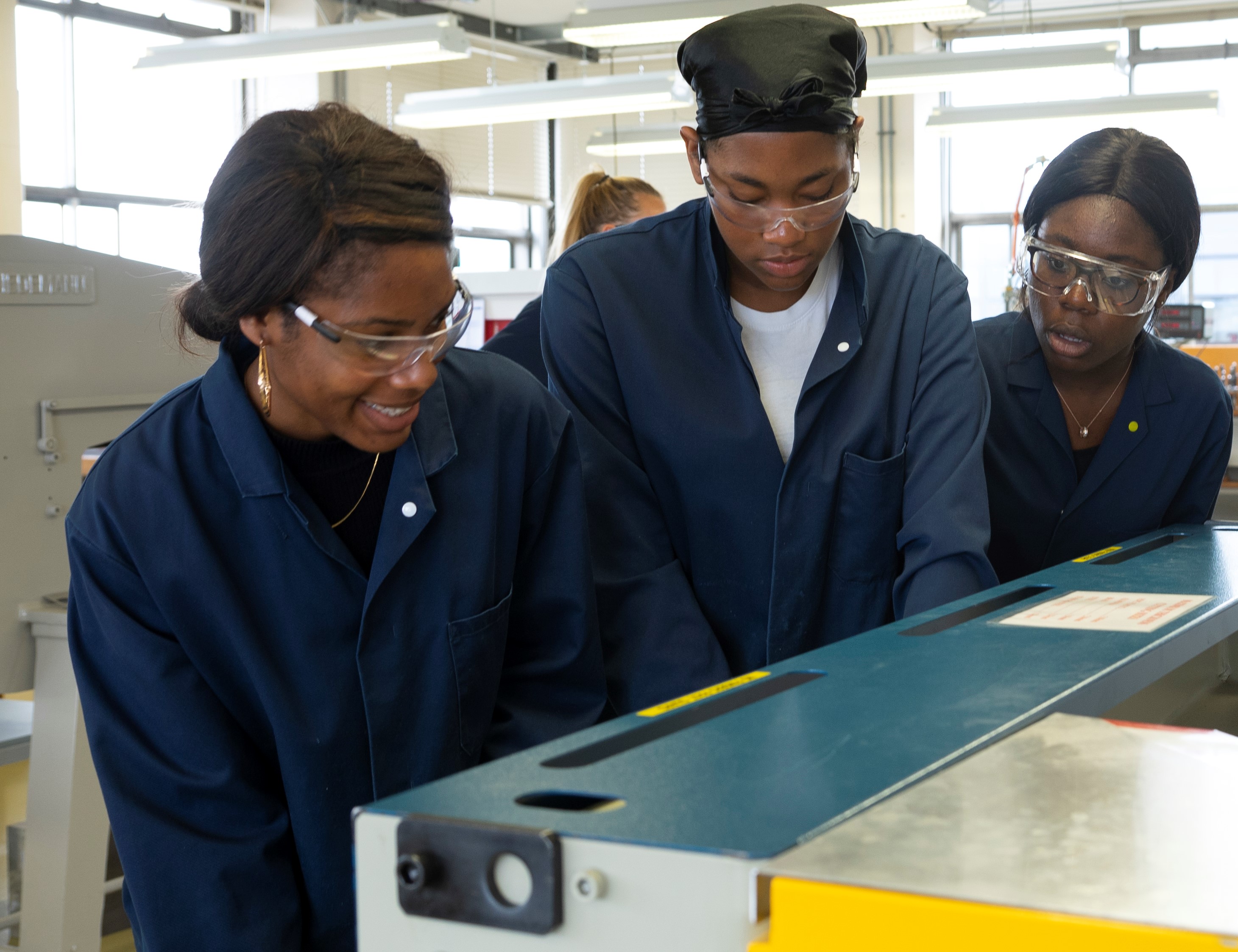 Three students in lab coats looking at a machine